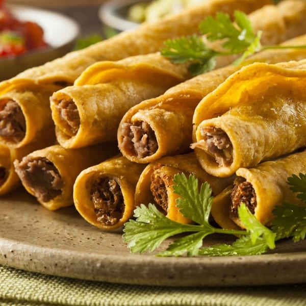 Close-up of golden-brown taquitos filled with meat, garnished with fresh cilantro on a rustic plate.