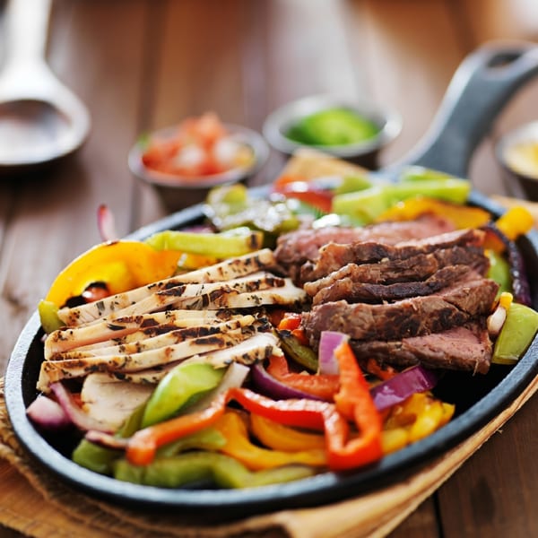 Sizzling chicken and steak fajitas with colorful bell peppers and onions in a cast iron skillet.